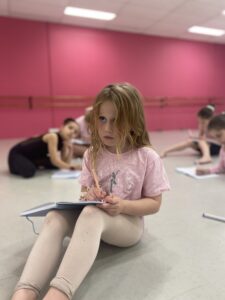 A young dancer focussing very hard on taking notes from the whiteboard.